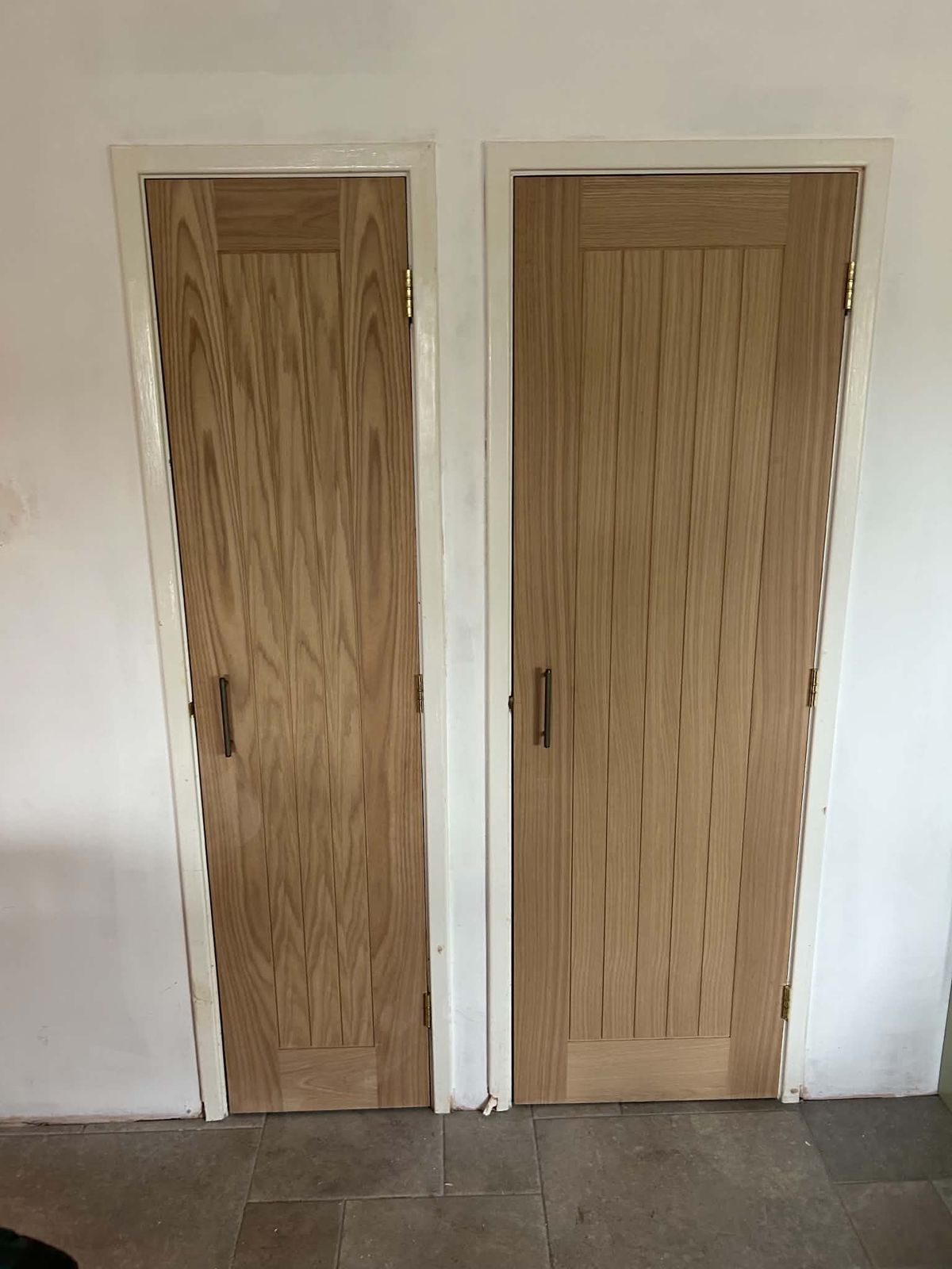 Two oak cottage-style internal doors side by side with white frames, on a tiled floor